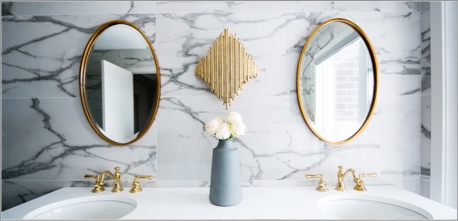 marble bathroom walls with two gold-rimmed mirrors and a white countertop sink